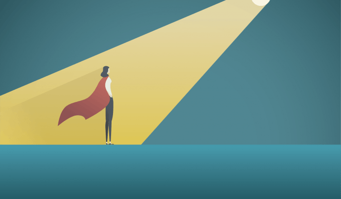 Businesswoman wearing a cape standing in a spotlight