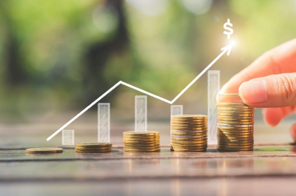 Stacks of coins increasing in size from left to right with a graph over top of them charting a revenue increase.