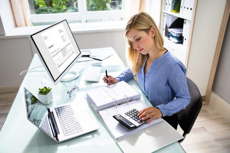 Young Businesswoman Calculating Bill With Computer And Laptop On Desk. Represents expense management.