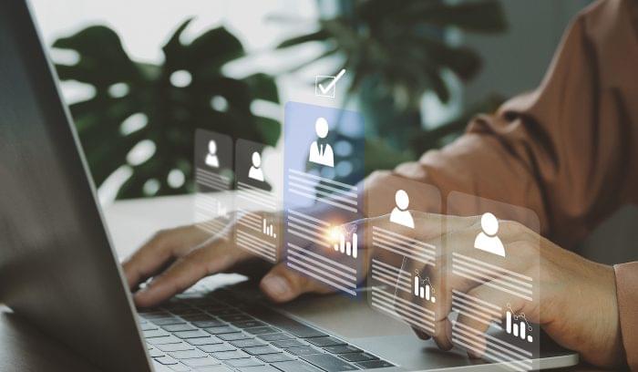 A row of virtual candidate profiles is superimposed on an image of a business professional typing on a laptop. Represents the resume screening process.