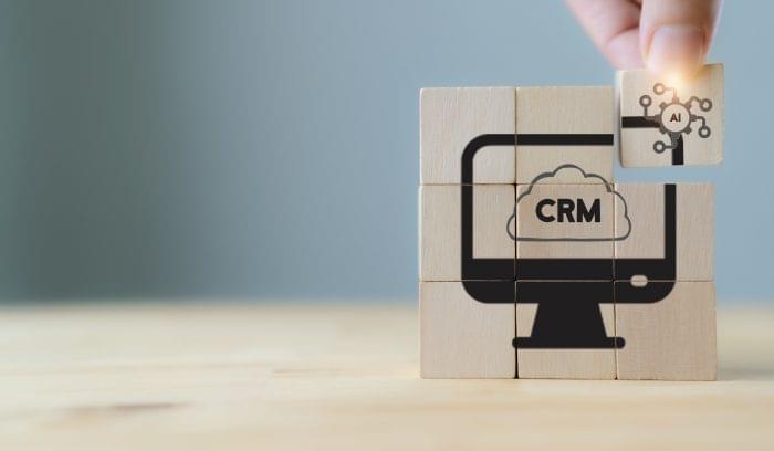 AI-CRM solution concept. Data driven marketing strategy with AI. For marketing plan, providing automated interaction to customer. Hand hold wooden cubes with AI-CRM icon on grey background, copy space.