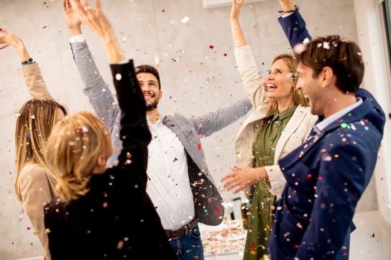 Group of excited business people celebrating and toasting with confetti falling in the office.