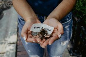 Woman holding a few coins with a paper written that says "Make a change".