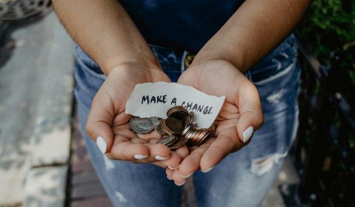 Woman holding a few coins with a paper written that says "Make a change".